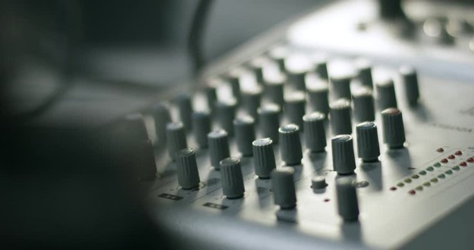 Audio mixer console with buttons. Camera slides past objects in foreground shallow depth of field. Part of recording studio. Sharp light and shallow depth of field. Slow motion.