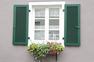 Fototapeta na wymiar Window with green shutters, on the windowsill, a potted with flowers