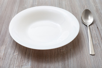 white deep plate and spoon on gray brown board