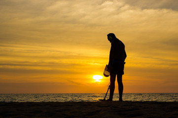 Treasure hunter with Metal detector on the sunset the beach