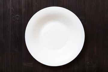 top view of white deep plate on dark brown table