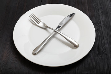 white plate with crossing knife, spoon on dark