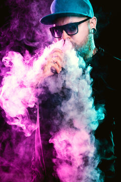 Men with beard  in sunglasses vaping and releases a cloud of vapor.
