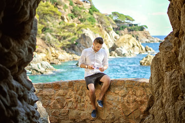 A handsome young man in the big cave, view from inside. Beutiful sea and island view on the background.