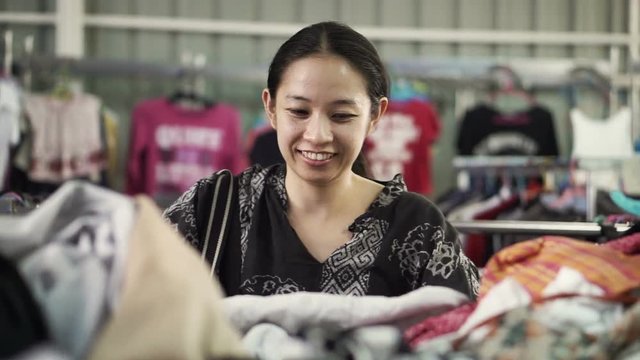 Happy Asian mixed race girl looking for good cheap clothes in sale bazaar