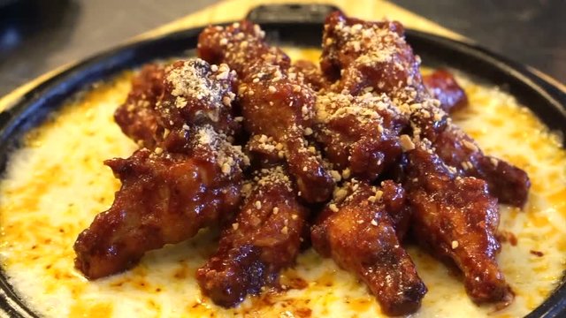 Spicy red sauce chicken drum sticks and wings serve with melting cheese on hot pan