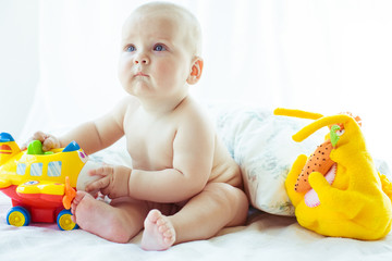 Boy with plump cheeks looks up while sitting on the bed with toy