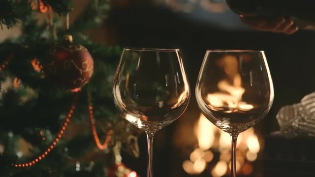 Pour the wine into the glasses on the background of the Christmas tree and fireplace. Christmas party