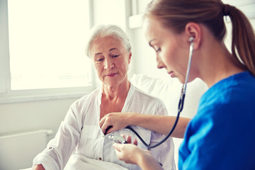 nurse with stethoscope and senior woman at clinic