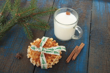 Obraz na płótnie Canvas milk with cinnamon in a transparent mug, waffles, cakes, tied with Christmas ribbon, anise on blue wooden background