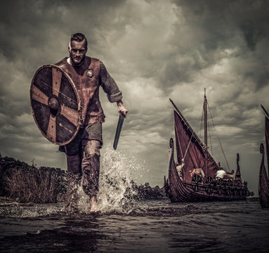 Viking warrior in attack, running along the shore with Drakkar on background
