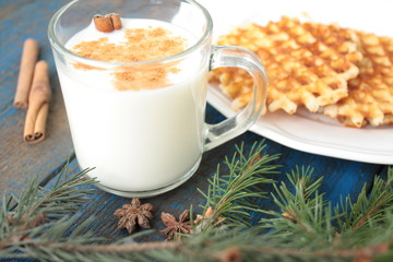 milk with cinnamon in a transparent mug, waffles, cakes, tied with Christmas ribbon, anise on blue wooden background