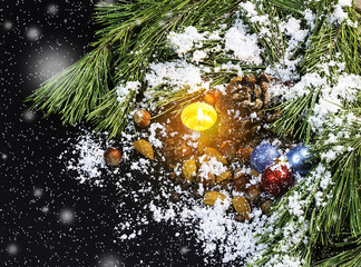 Pine branches, candle, Christmas tree decorations, nuts, the pine cone in snow on a black...