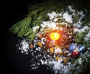 Fototapeta na wymiar Pine branches, candle, Christmas tree decorations, nuts, the pine cone in snow on a black background 