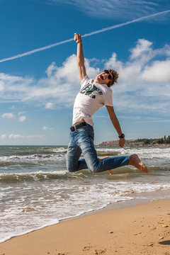 Young man jumping on the beach in the oncoming waves