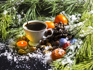 White vintage cup with hot coffee, nuts, tangerines, a candle, pine branches on a black background