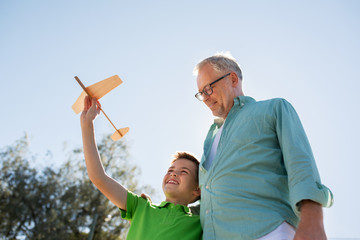 senior man and boy with toy airplane over sky