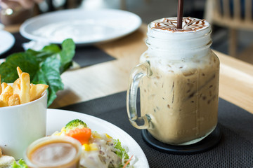 A glass of ice cappuccino art with foods on table