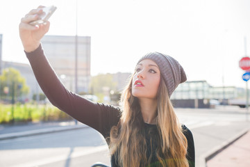 Half length of young handsome caucasian blonde hair woman wearing hat taking selfie with smartphone handhold - vanity, technology, social network concept