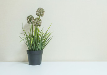 Closeup artificial plant with flower on black pot on blurred wooden desk and wall textured background in room with copy space