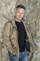 Outdoor male portrait. Man standing near rock wall and looking u