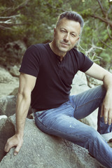 Naklejka na ściany i meble Outdoor male portrait. Man sitting on rocks near mountain river,