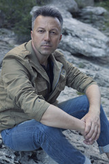 Outdoor male portrait. Handsome middle-aged man sitting on rocks