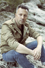 Obraz premium Outdoor male portrait. Handsome middle-aged man sitting on rocks