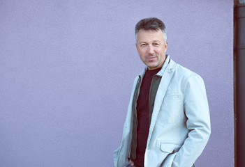 Handsome cheerful mid adult man posing over violet wall. Outdoor