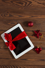 tablet with red  bow,  gift  wooden background, concept Christma