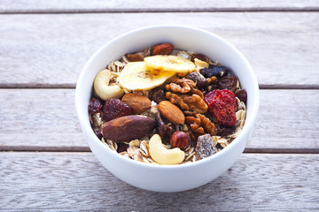 Close up of a healthy bowl of muesli with dried fruit and nuts on a wooden background.