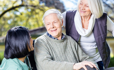 Elder couple in rehab clinic garden smiling with asian nurse