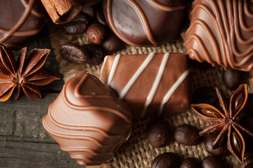 Assortment of dark, white and milk chocolate stack, chips. Chocolate and coffee beans on rustic wooden sacking background. Spices, cinnamon. Selective macro focus. Chocolates background. Sweets