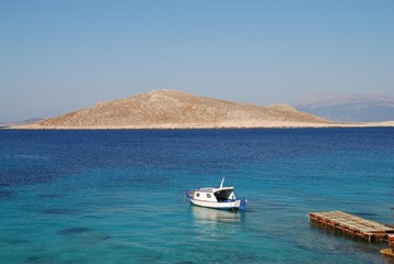 Fototapeta na wymiar A small boat moored near Ftenegia beach at Emborio on the Greek island of Halki. The uninhabited island of Nissos is in the background.