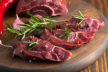 Close-up of raw fresh marble meat on board with condiments on white background. Chili pepper, rosemary, salt and black pepper. Ready for steak.