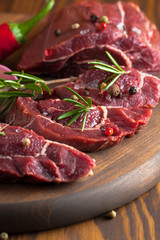 Close-up of raw fresh marble meat on board with condiments on white background. Chili pepper, rosemary, salt and black pepper. Ready for steak.