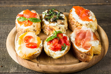 Various types of tapas. Italian tasty tomato, mushrooms, prosciutto, ham, salmon and cheese bruschetta. Antipasti with vegetables, herbs and oil on grilled ciabatta and baguette.