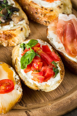 Various types of tapas. Italian tasty tomato, mushrooms, prosciutto, ham, salmon and cheese bruschetta. Antipasti with vegetables, herbs and oil on grilled ciabatta and baguette.