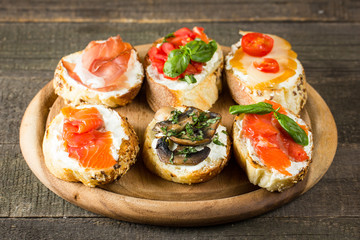 Various types of tapas. Italian tasty tomato, mushrooms, prosciutto, ham, salmon and cheese bruschetta. Antipasti with vegetables, herbs and oil on grilled ciabatta and baguette.