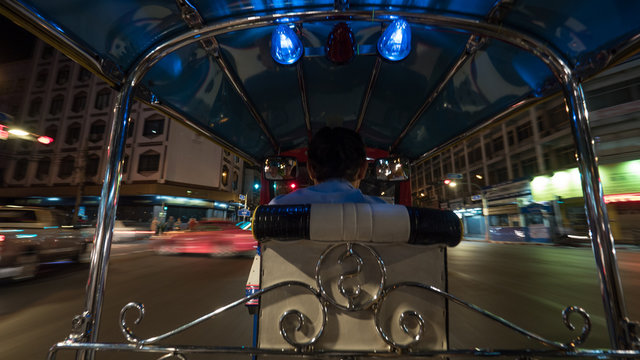 Man Driving Tuktuk Taxi On The Roads Of Night Bangkok, Thailand. View From Passenger Seat