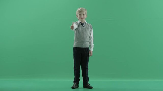 schoolboy is showing thumbs up and smiling on green screen background