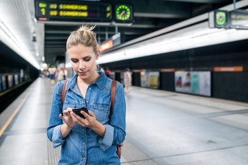 Woman at the underground platform with smartphone texting