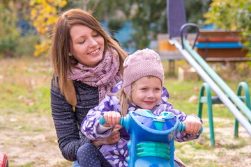 Little girl with her mother sitting at the children's home-made motorcycle in the yard