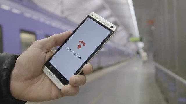 man holding a smartphone that connects to wifi at a train station