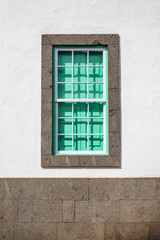 green shutter behind bars on a white wall surrounded by brick