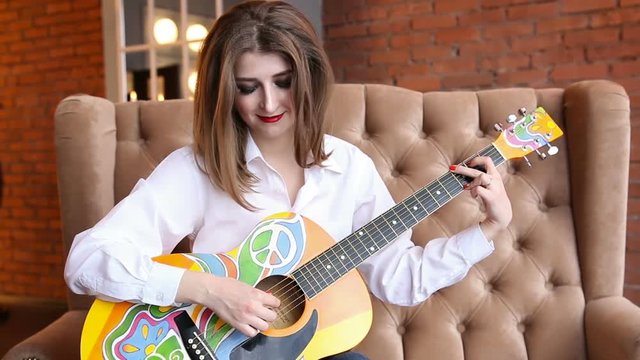 Girl in a white shirt plays guitar in hippie style