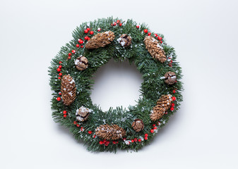Christmas wreath of fir branches decorated with ilex, cypress cones, pine cones and artificial snow on white background
