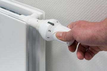 Hand bedient ein Thermostat an einer Heizung