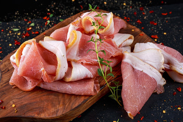 Raw smoked bacon slices on wooden board which herbs