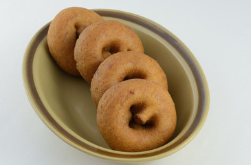 Plain breakfast donuts in brown bowl against white background